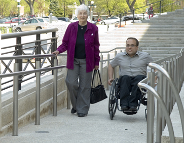 A person walking beside another person in wheelchair